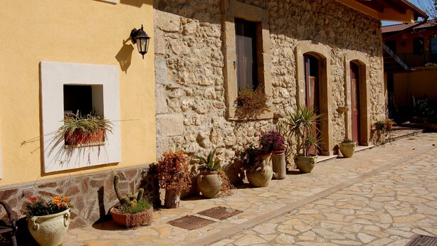 A stone building with a yellow facade, multiple windows, and potted plants along the exterior. - Il Giardino del sole (Carlentini)