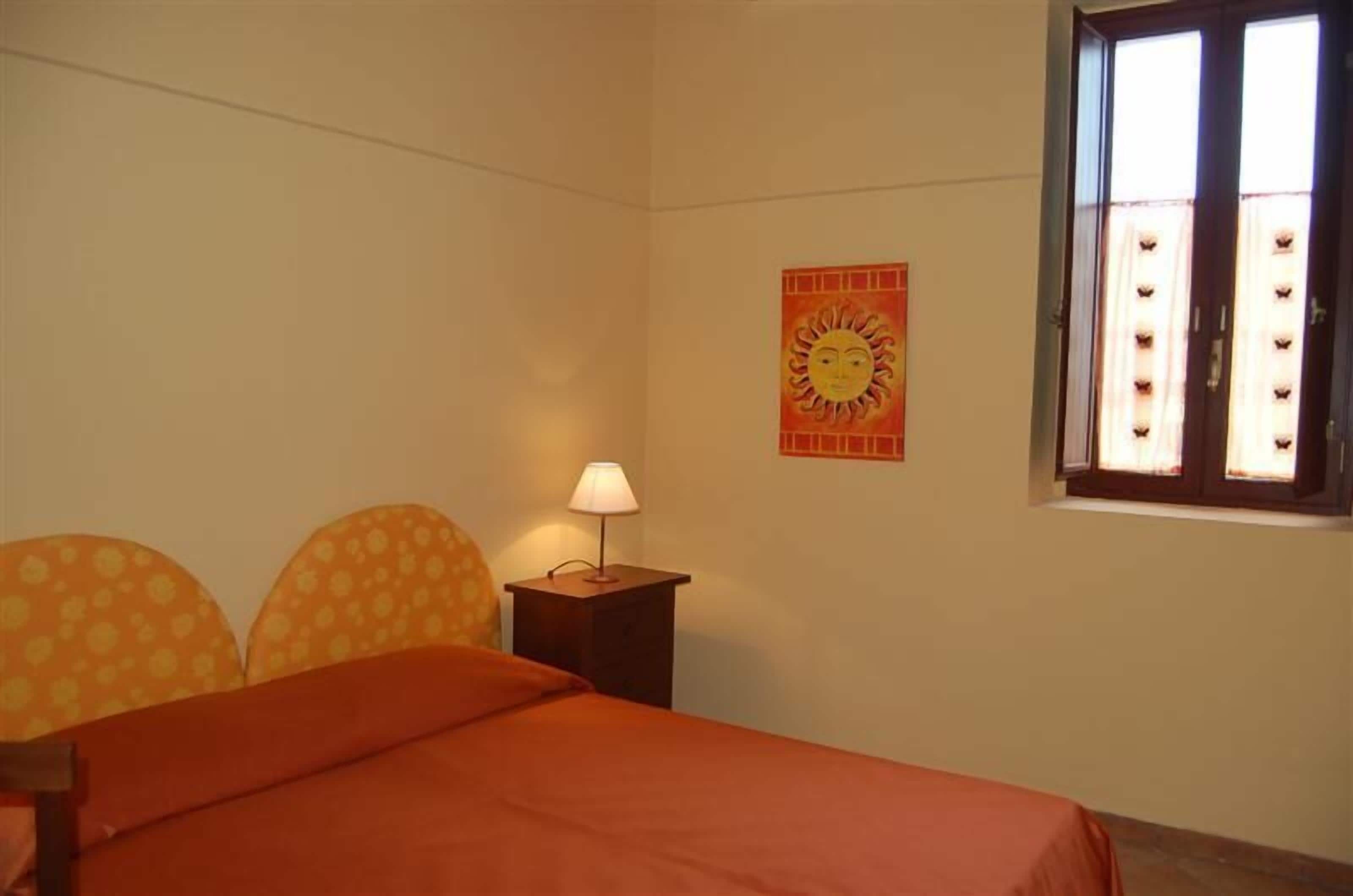 A bedroom with a bed, a nightstand with a lamp, a window with curtains, and a wall decoration.