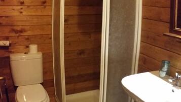 Un baño pequeño con paneles de madera, con cabina de ducha, inodoro y lavabo.