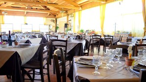 A restaurant with multiple tables set for dining, featuring a rustic wooden interior and large windows with curtains. - Il Giardino del sole (Carlentini)