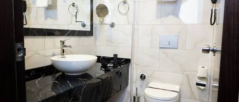 A modern bathroom with a white sink, black marble countertop, a toilet, and a shower area.