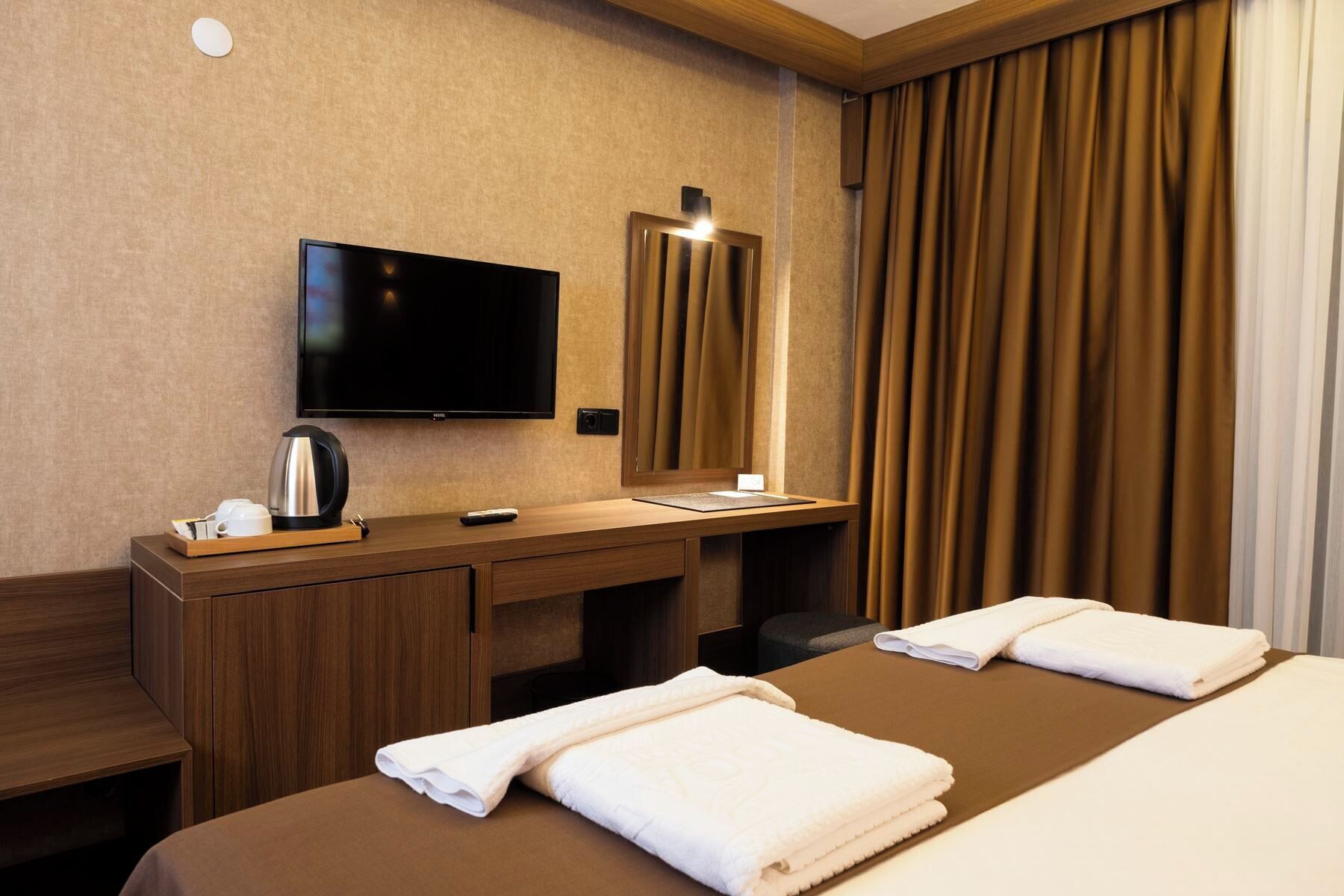 A hotel room with a bed, a desk with a flat-screen TV, a mirror, a coffee maker, and towels.