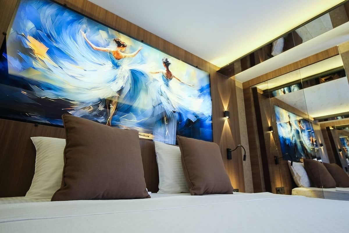 Una habitación de hotel con un cuadro abstracto grande en la pared, una cama con muchas almohadas y un espejo que refleja la habitación.
