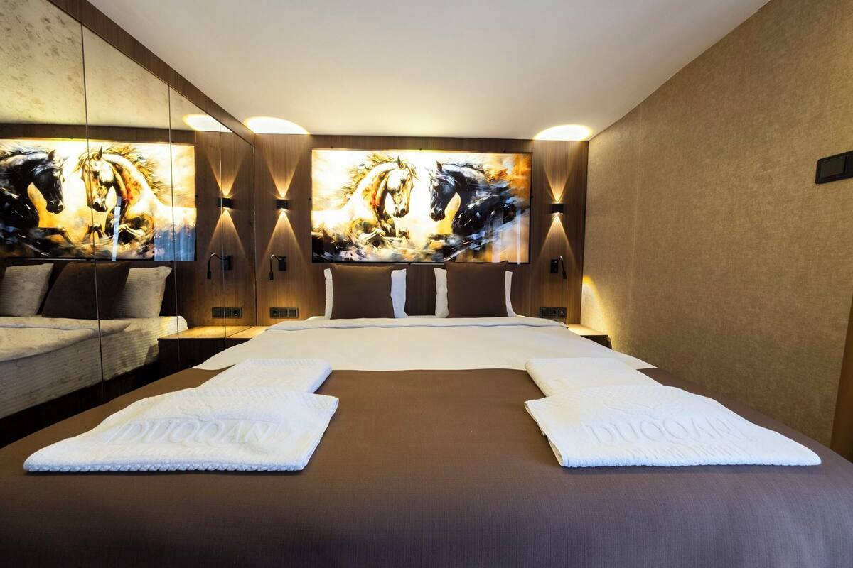 Habitación de hotel con una cama grande, dos televisores montados en la pared y un espejo.