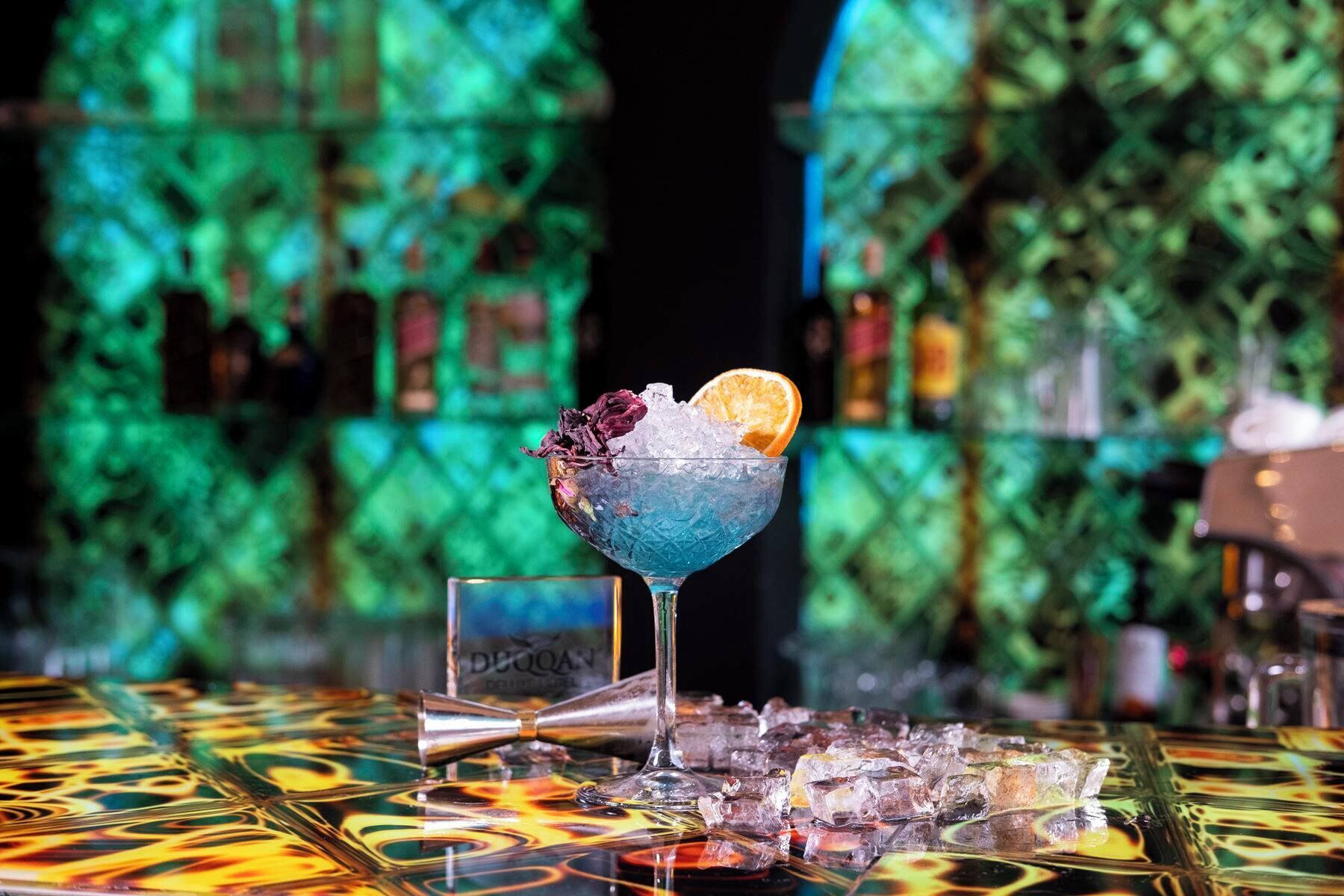 A cocktail in a glass with ice and a slice of orange on a bar counter.
