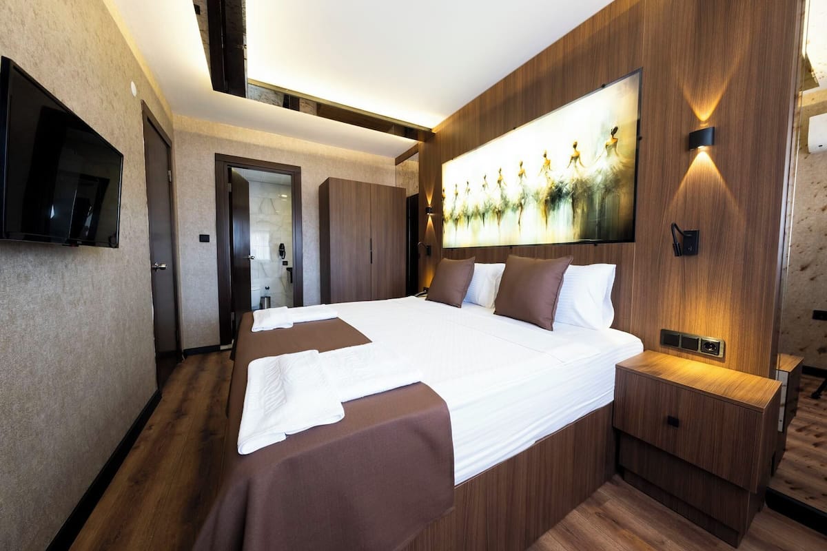 Una habitación de hotel moderna con una cama grande, paneles de madera, un televisor de pantalla plana y un cuadro en la pared.