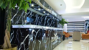 A reception desk with a black marble design, a digital clock, and the name 'DUOQAN DELUXE HOTEL' visible. - Duqqan Deluxe Hotel (Kusadasi)