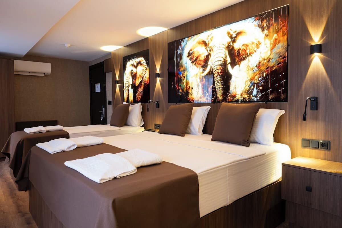 Habitación de hotel con una cama grande, dos mesitas de noche y un televisor montado en la pared mostrando una imagen dinámica.