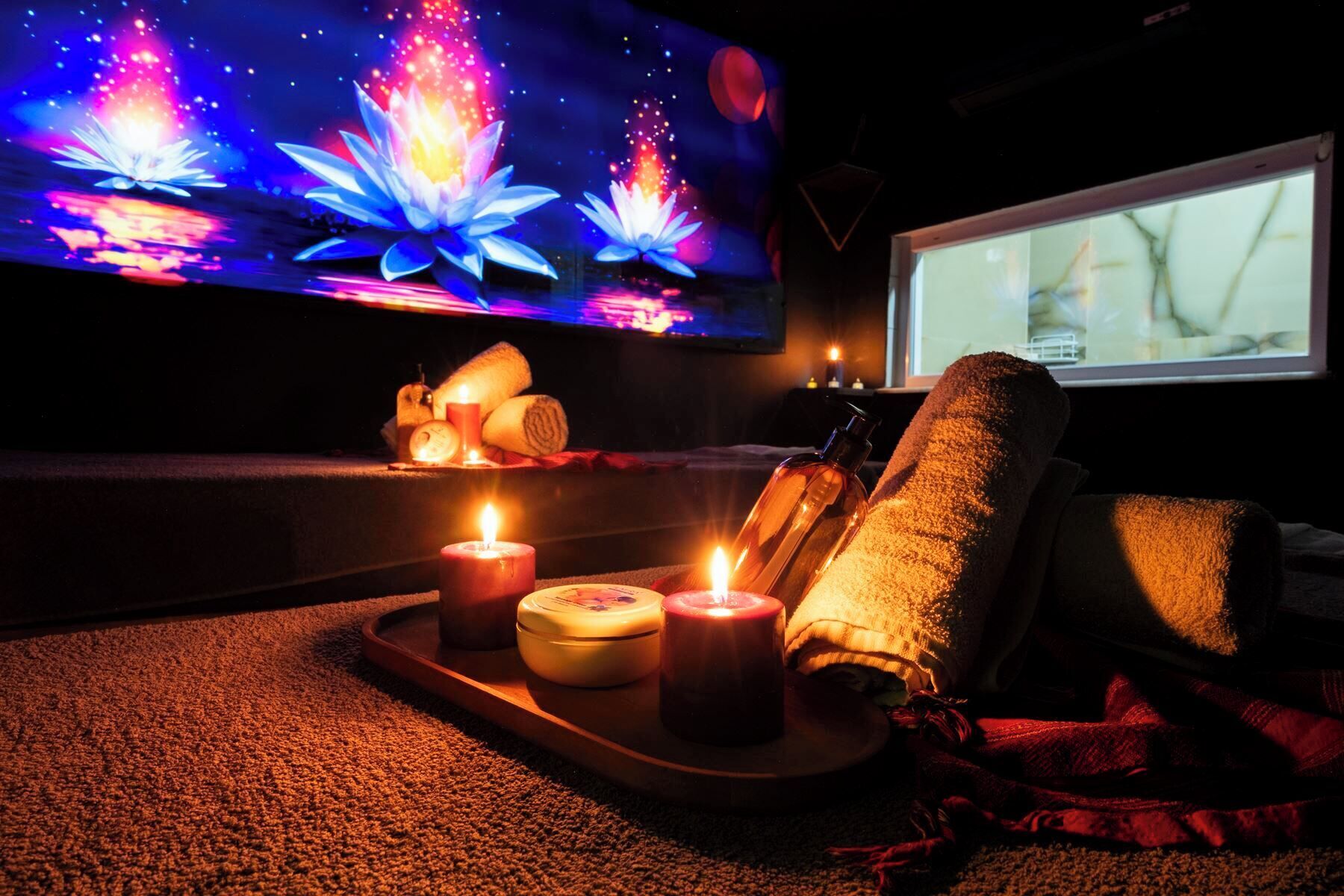 A cozy room with a massage chair, candles, and a tray with candles and a bottle, suggesting a relaxing environment.