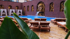 A poolside area with wooden lounge chairs, a brick wall with arched windows, and a statue. - Duqqan Deluxe Hotel (Kusadasi)