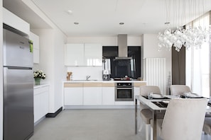 A modern kitchen with white cabinetry, stainless steel appliances, and a dining area with a chandelier. - Platform Merter Suites (Istanbul)