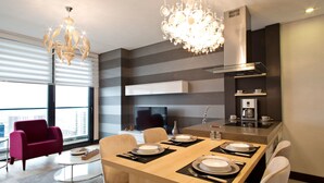 A modern dining area with a wooden table set for four, a chandelier, and a kitchen with a stove and coffee maker. - Platform Merter Suites (Istanbul)