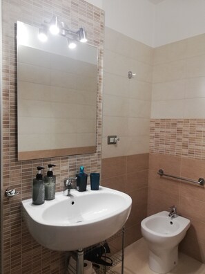 A bathroom with a white sink, a mirror, a bidet, and toiletries on the counter. - B&B Li Figuli (Lecce)