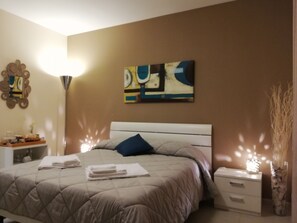 A bedroom with a bed, bedside tables, a nightstand, and wall art. - B&B Li Figuli (Lecce)