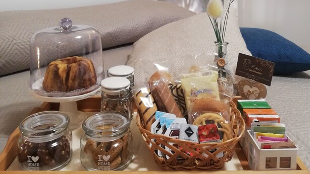 A neatly arranged breakfast tray with pastries, a cake, and jars of spreads on a bed with pillows and a painting on the wall. - B&B Li Figuli (Lecce)