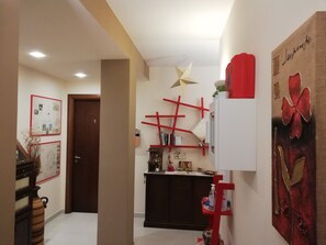 A hallway with a wooden door, a red shelf with various items, a star decoration on the ceiling, and a large painting on the wall. - B&B Li Figuli (Lecce)
