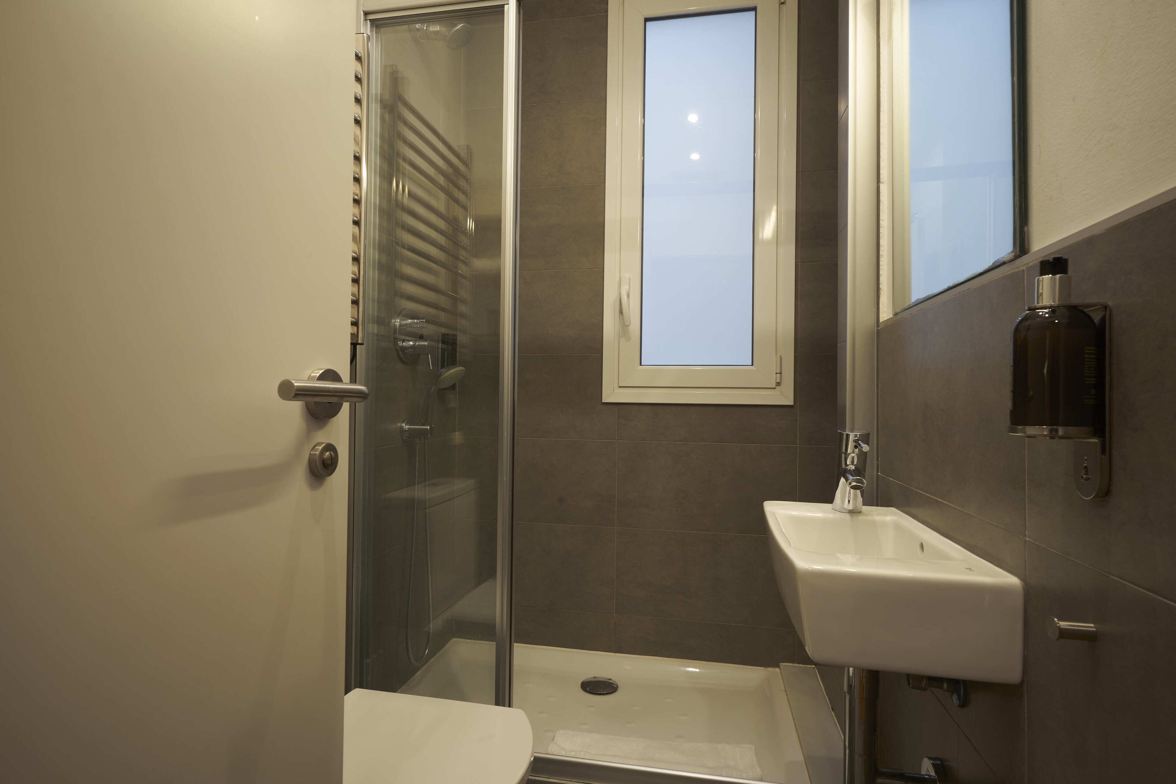 Ein Badezimmer mit Duschkabine aus Glas, einem weißen Waschbecken und einem Fenster über dem Waschbecken.