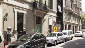 A street view of a building with multiple windows, a visible entrance, and parked cars. - Bonavista Apartments - Passeig de Gracia (Barcelona)