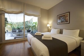 A hotel room with a bed, a bedside table, a lamp, and a view of an outdoor area with plants and a patio. - Bonavista Apartments - Passeig de Gracia (Barcelona)