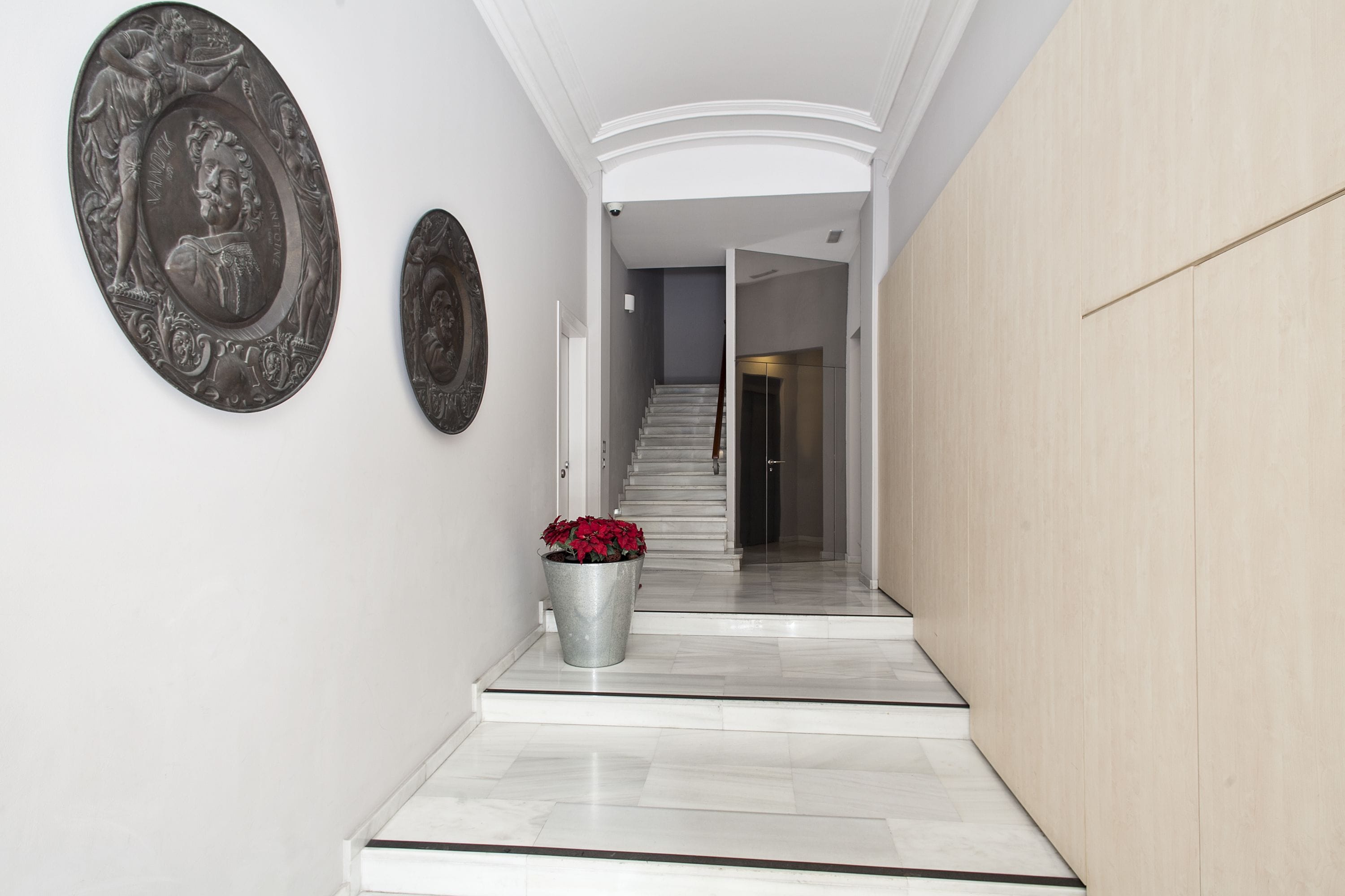 Um corredor com piso de mármore, escadaria e duas placas decorativas fixadas na parede.
