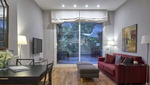 A modern living room with a red sofa, a grey ottoman, a dining table with chairs, a TV, and a large window with a view of the outdoors. - Bonavista Apartments - Passeig de Gracia (Barcelona)