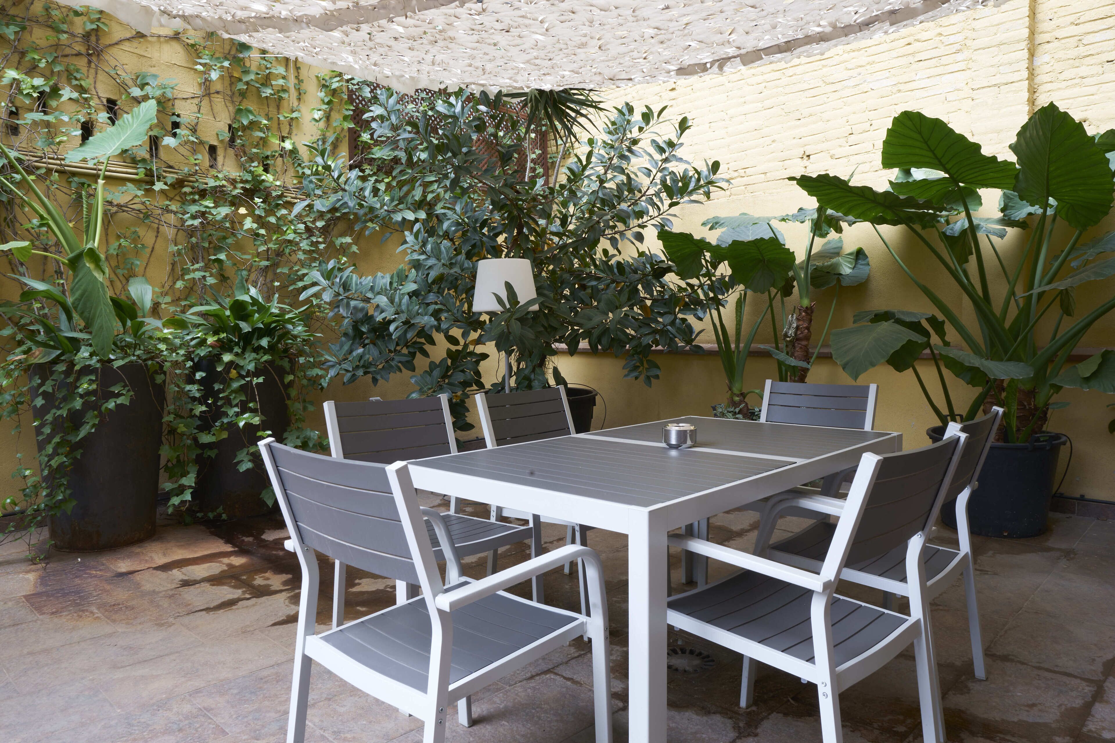 A patio with a table and chairs, surrounded by potted plants and a yellow wall.