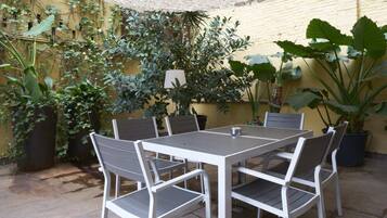 A patio with a table and chairs, surrounded by potted plants and a yellow wall.