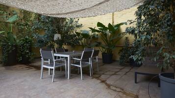 Un patio al aire libre con una mesa y sillas, rodeado de macetas con plantas y una pared amarilla.