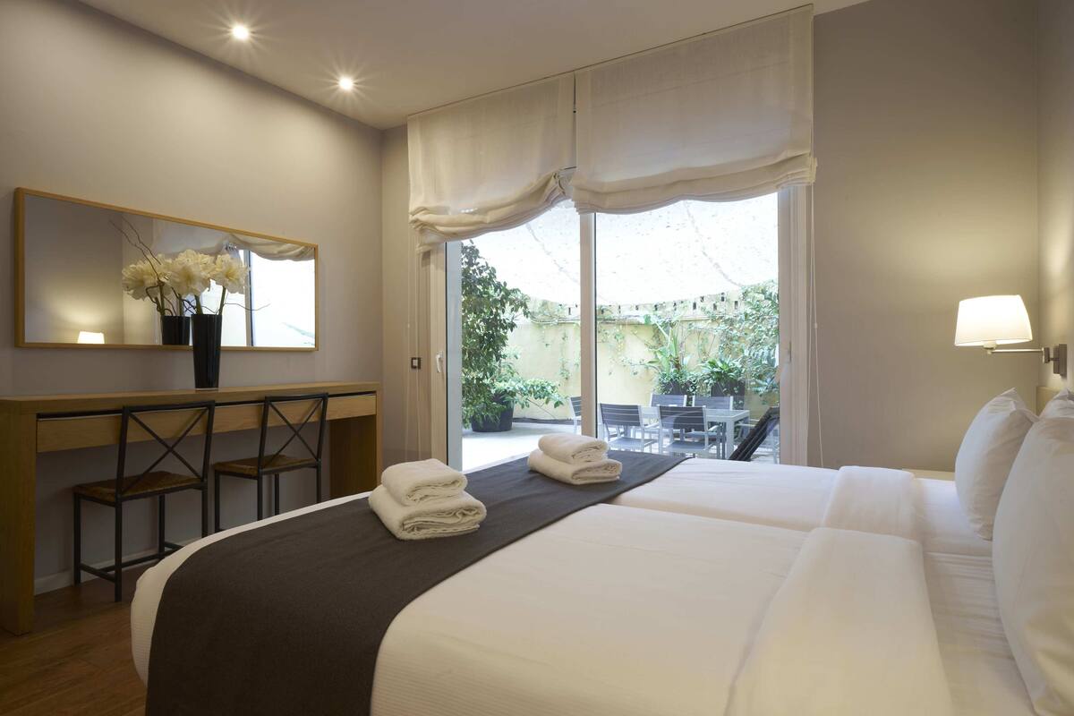 A hotel room with a large bed, a desk with chairs, a mirror, and a view of the outdoor patio.