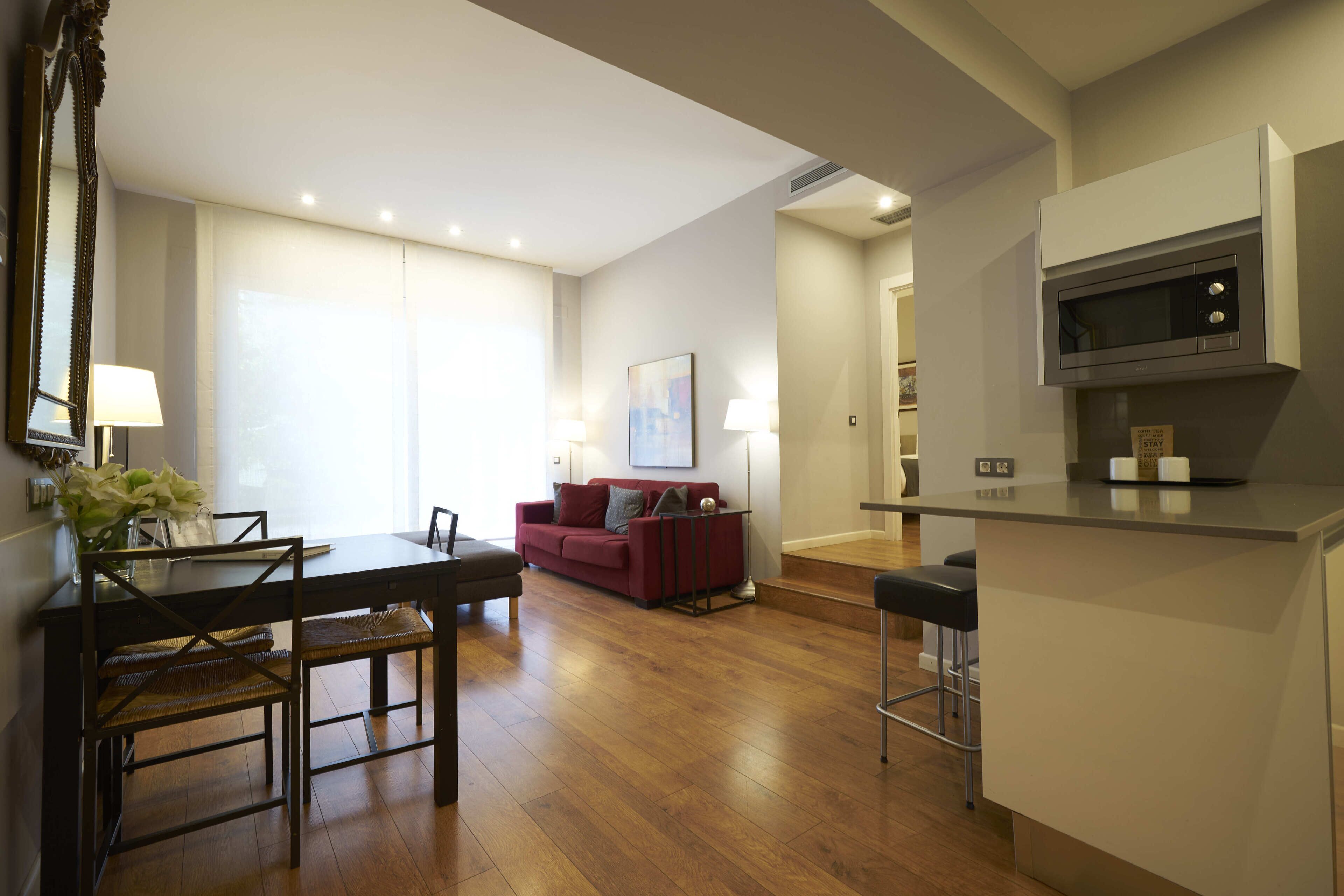 A modern living room with a dining area, a red sofa, and a kitchen with a microwave.