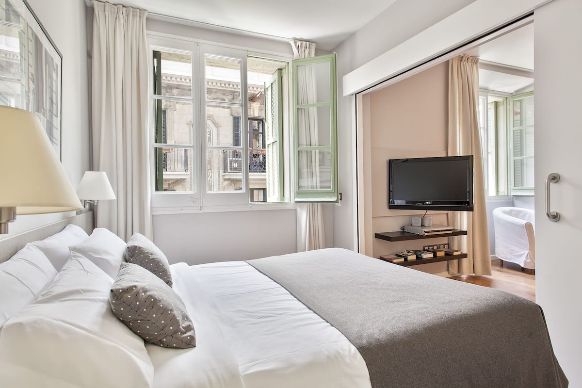 A hotel room with a bed, a television, a window with curtains, and a view of the outside building.