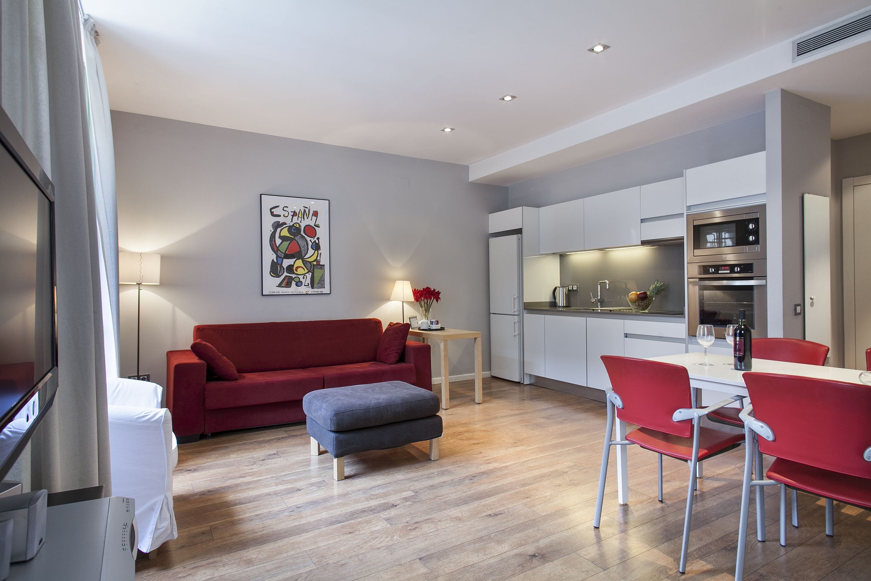 Un salon moderne avec un canapé rouge, un pouf gris et des fauteuils rouges disposés autour d’une table blanche.