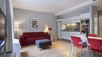 Un salon moderne avec un canapé rouge, un pouf gris et des fauteuils rouges disposés autour d’une table blanche.