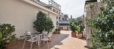A courtyard with a tiled floor, a table with chairs, and potted plants.