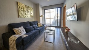 A modern living room with a dark blue sofa, a glass coffee table, and a decorative wall piece. - Bonavista Apartments - Virreina (Barcelona)