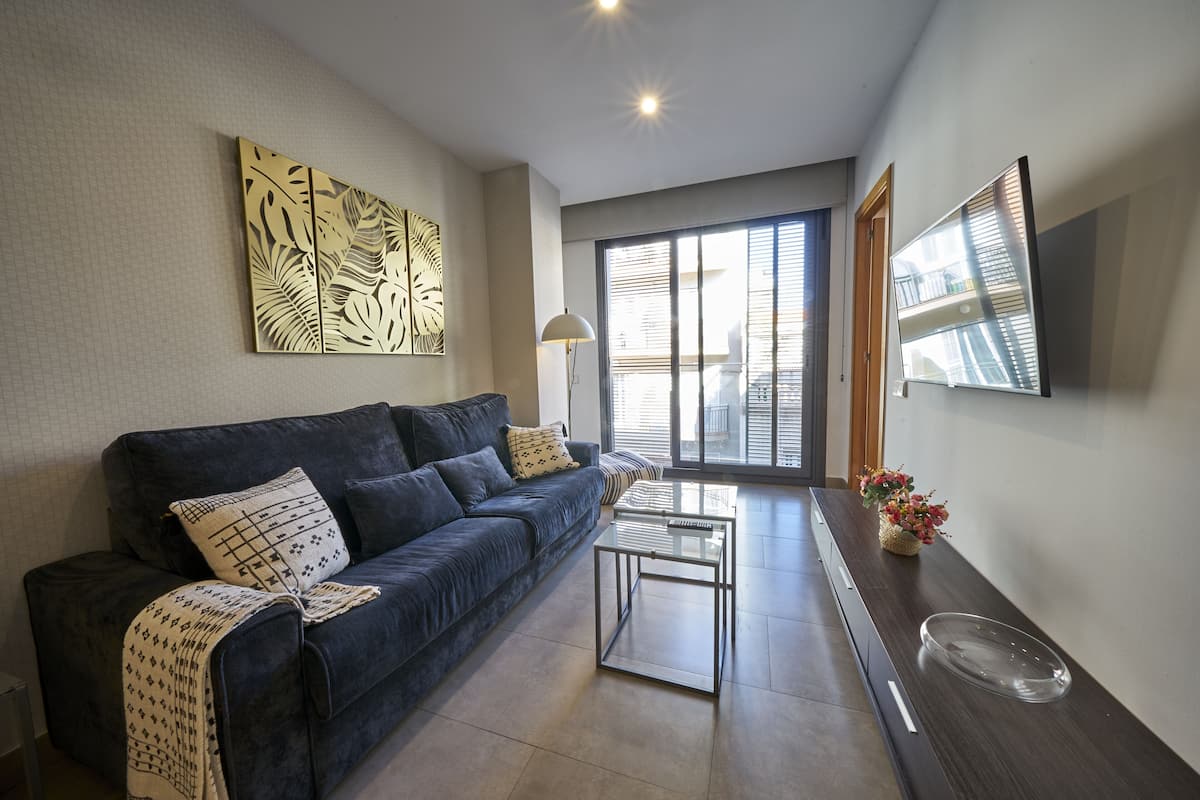 A modern living room with a dark blue sofa, a glass coffee table, and a decorative wall piece.