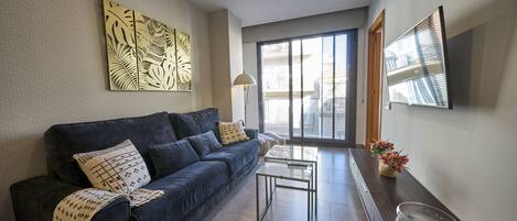 A modern living room with a dark blue sofa, a glass coffee table, and a decorative wall piece.