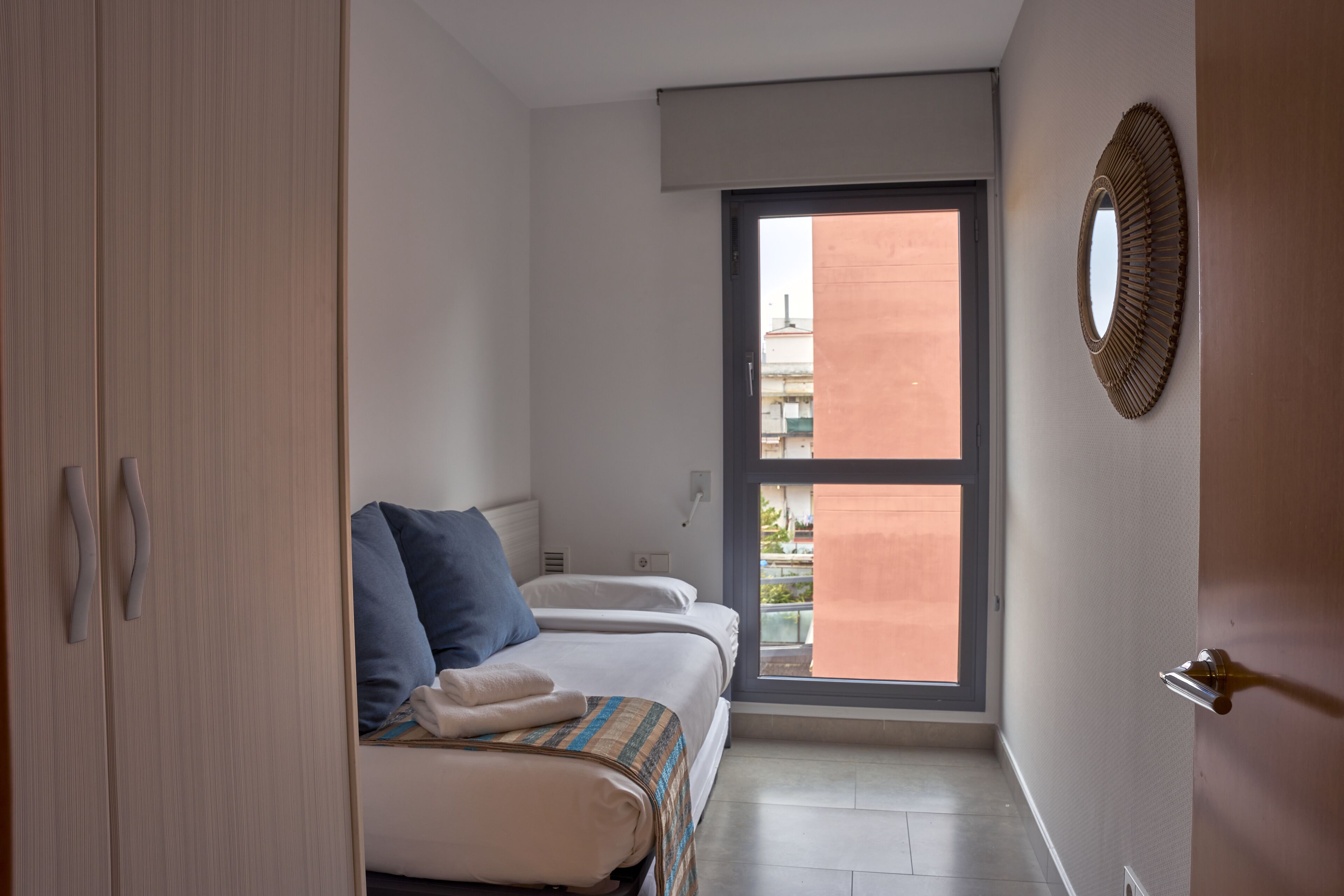 Une chambre à coucher comprenant un lit, une armoire, une fenêtre et un miroir fixé au mur.