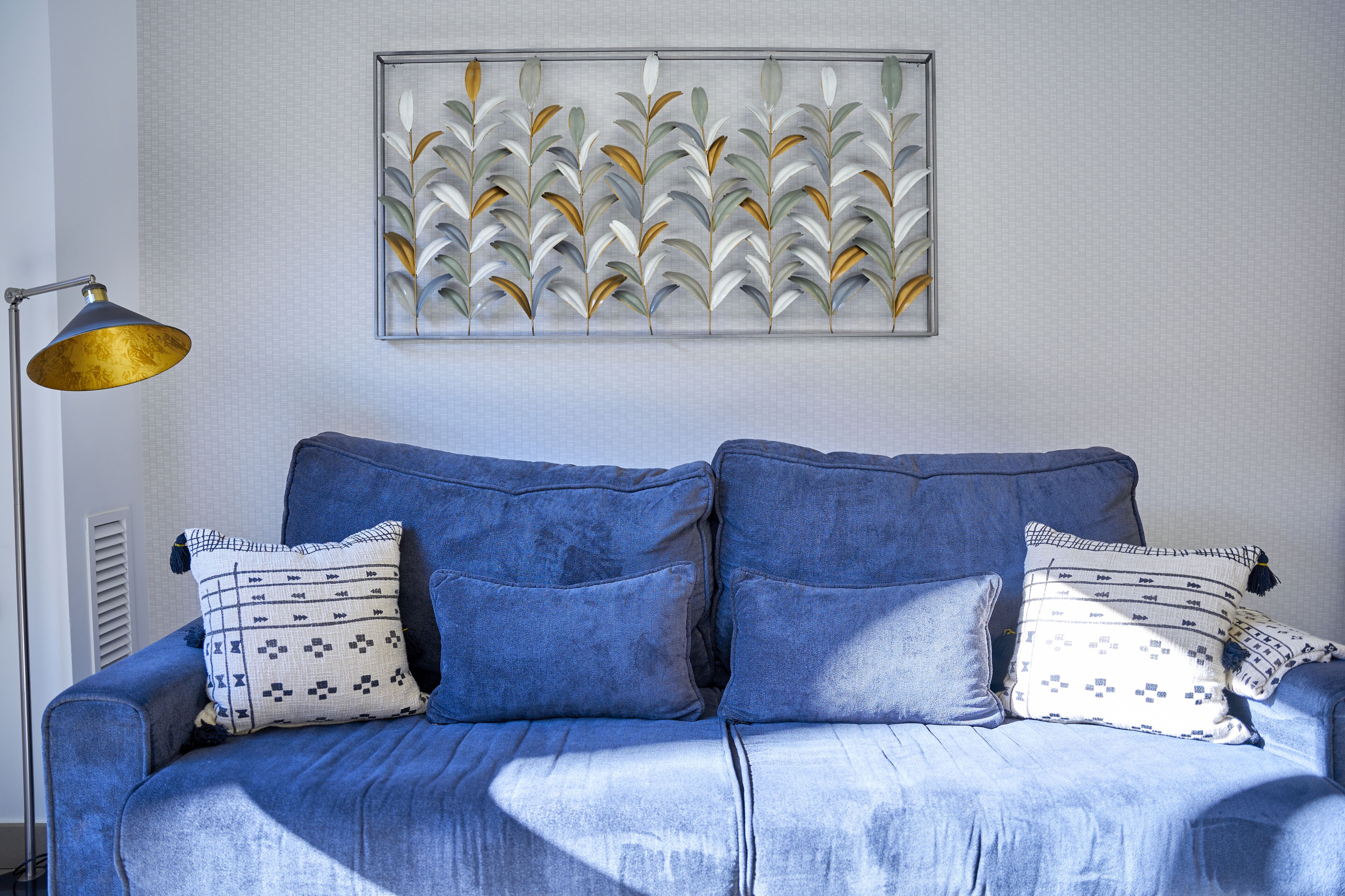 Un sofá azul con almohadones estampados, una obra de arte abstracta colgada en la pared y una lámpara de pie.