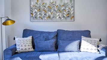 Un sofá azul con almohadones estampados, una obra de arte abstracta colgada en la pared y una lámpara de pie.