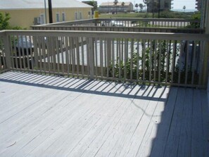 A wooden deck with a white railing, overlooking a parking area and buildings in the background.