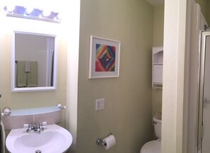 A bathroom with a white sink, a mirror, a toilet, and a colorful abstract painting on the wall.