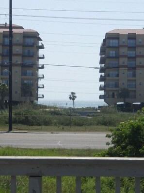 A view of two multi-story residential buildings with balconies, a clear sky, and a palm tree in the distance.