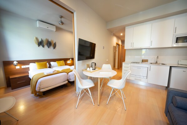 A modern hotel room with a bed, bedside table, and a small dining area with chairs. - Bonavista Apartments - Eixample (Barcelona)