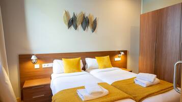 A hotel room with two beds, a wooden wardrobe, a nightstand, and wall-mounted decor.