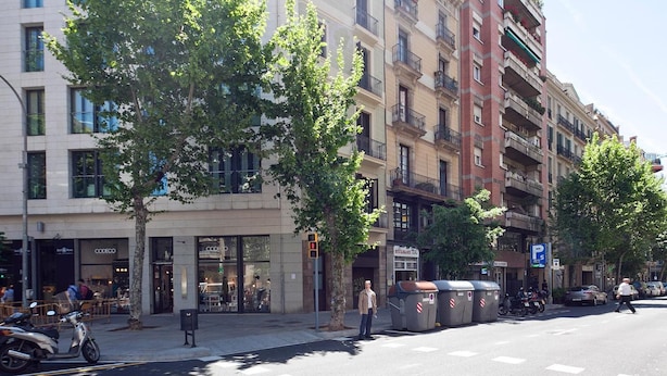 Vista de la calle con edificios de varios pisos, un paso de peatones y vehículos estacionados.