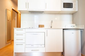 A compact kitchen with white cabinets, a microwave, a toaster, and a refrigerator. - Bonavista Apartments - Eixample (Barcelona)