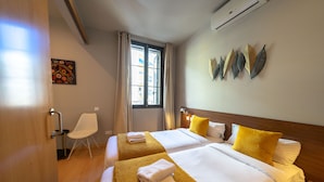 Habitación de hotel con dos camas, una ventana con cortinas, una silla y decoración en la pared.