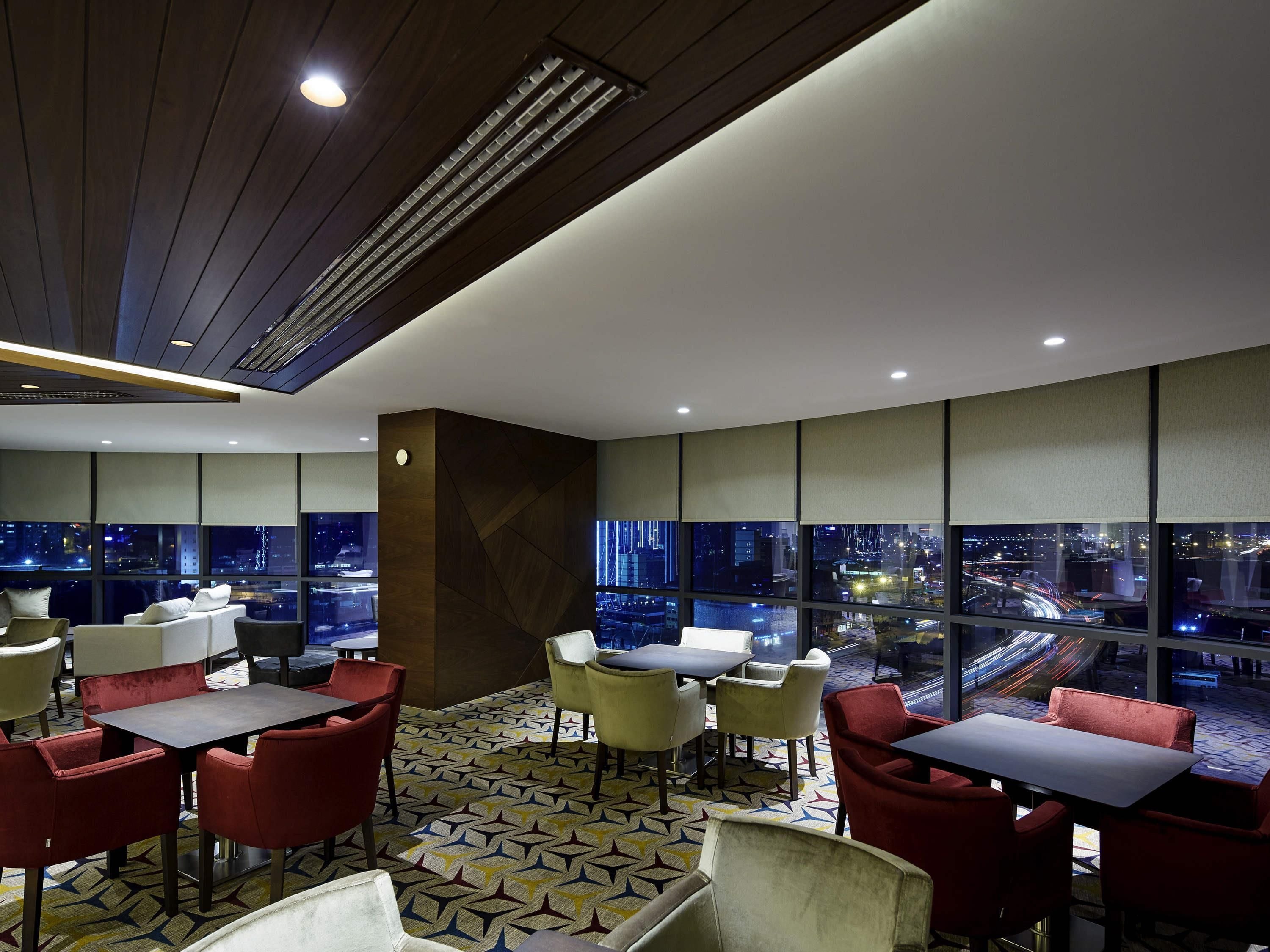 A modern dining area with tables and chairs, large windows offering city views, and a patterned floor.