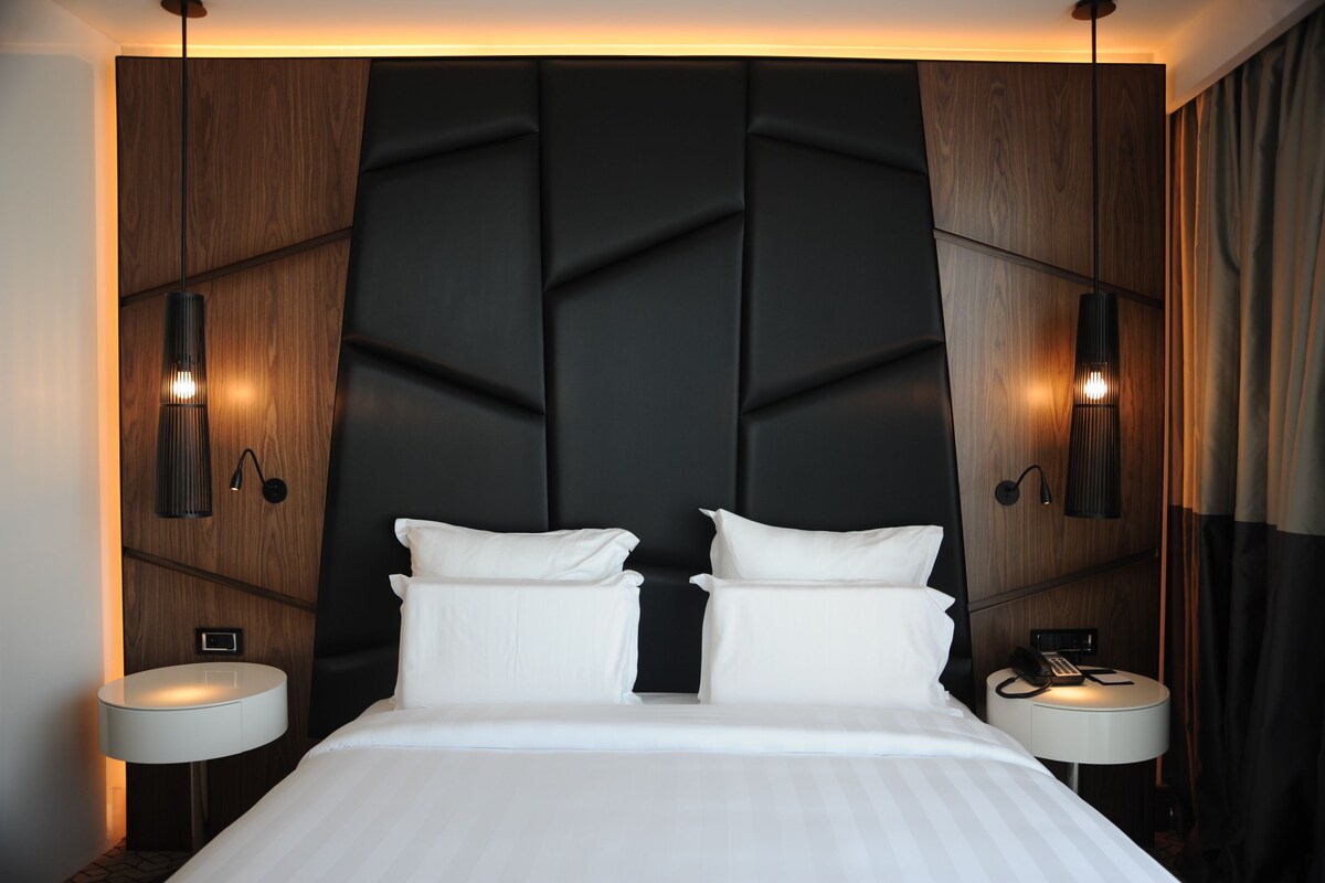 Une chambre d’hôtel moderne dotée d’un grand lit, de deux tables de chevet, d’un téléphone fixé au mur et d’une tête de lit intégrée.